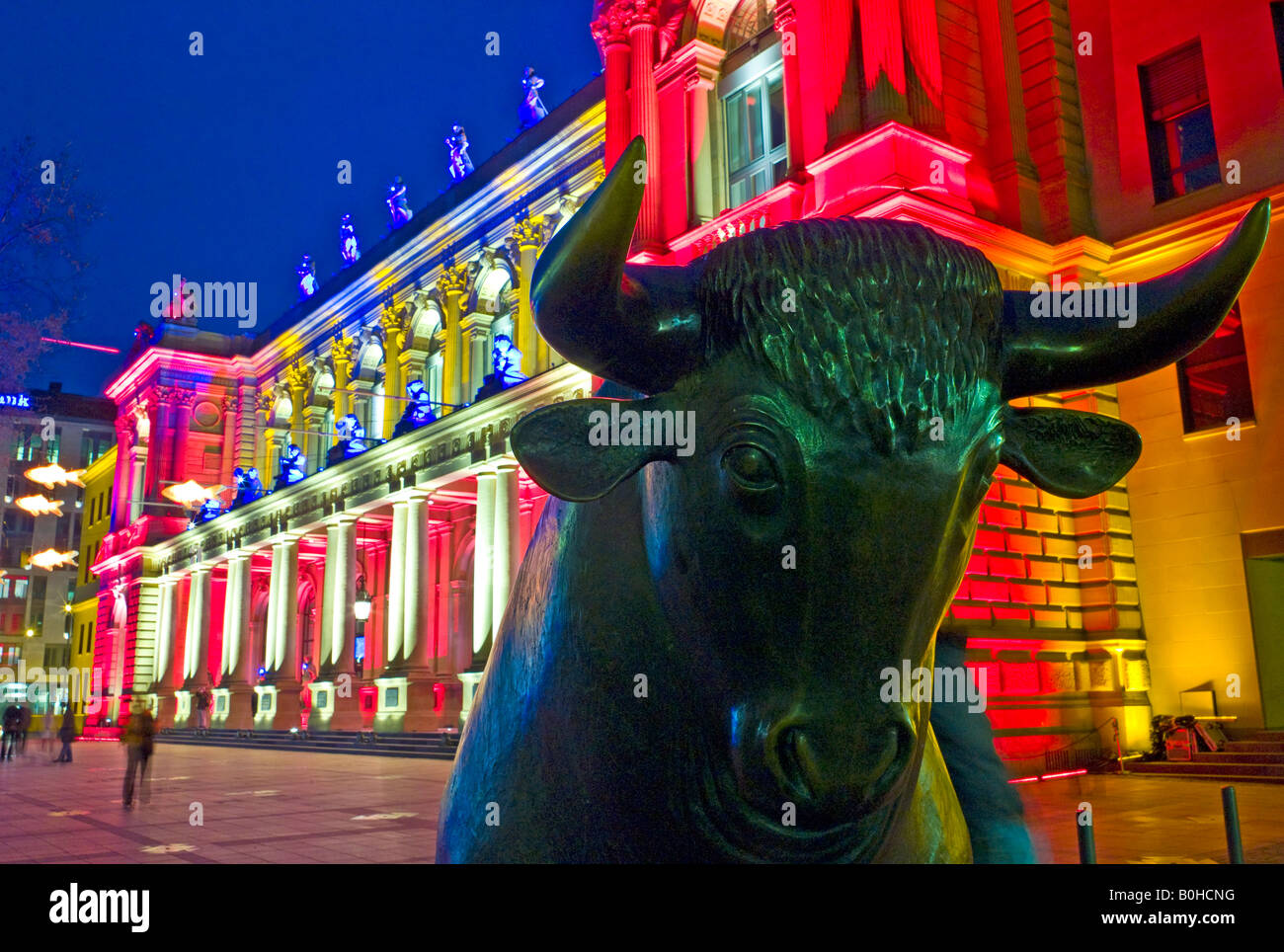 The bull of the Bull and Bear in front of the brightly lit Frankfurt Stock Exchange at night, illuminated by multicoloured spot Stock Photo