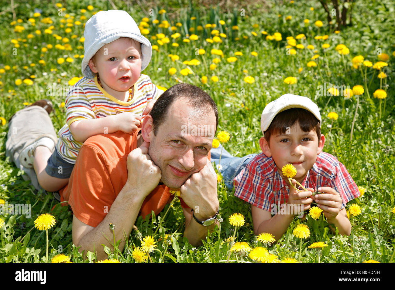 Father, Gaudenz Huggel, and his two sons lying on a dandelion meadow, Arlesheim, Baselland, Switzerland Stock Photo