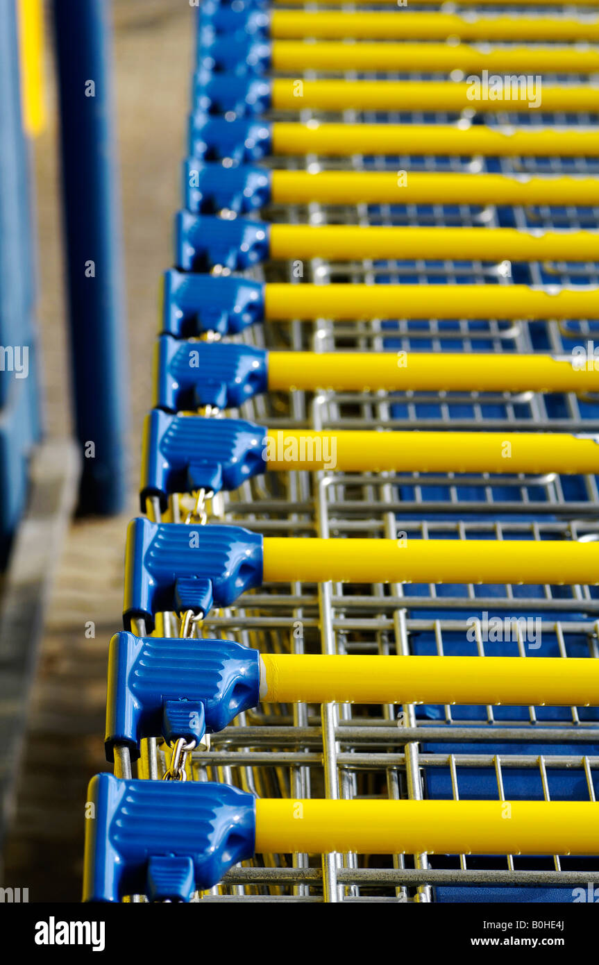 Blue and yellow shopping carts or trolleys stacked at a supermarket in Eckental, Middle Franconia, Bavaria, Germany Stock Photo