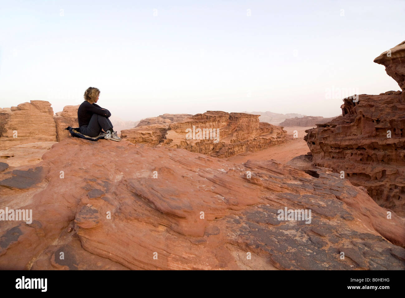 Woman sitting on a rock ledge looking off into the distance, Wadi Rum, Jordan, Middle East Stock Photo