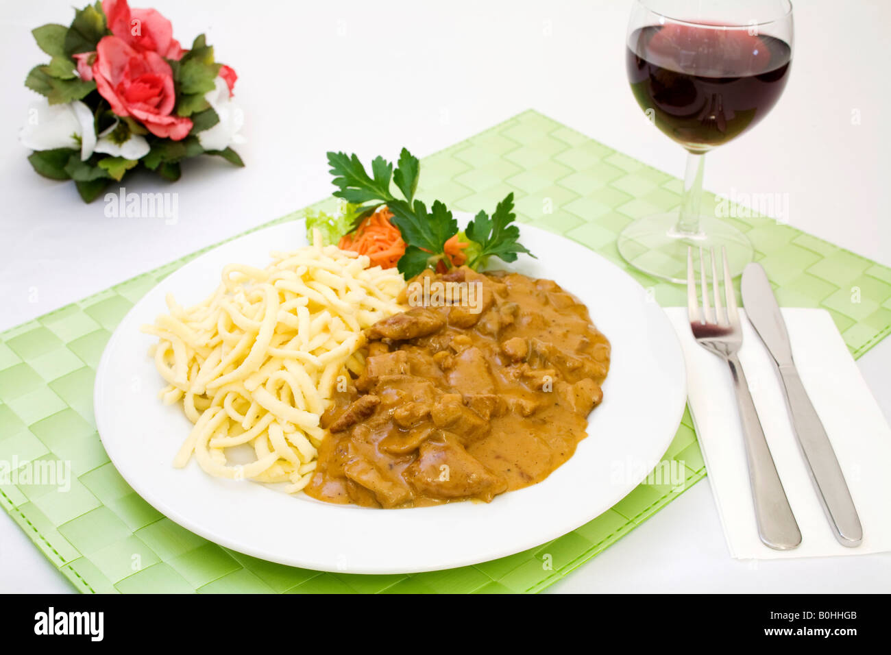 Zurich style pork filet strips with gravy served with spaetzle, fresh boiled egg noodles and a glass of red wine Stock Photo