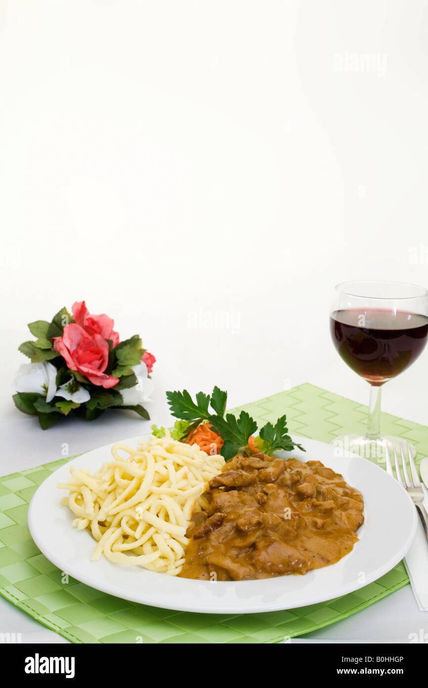 Zuercher Geschnetzeltes, Zurich style pork filet strips with gravy served with spaetzle, fresh boiled egg noodles and a glass o Stock Photo