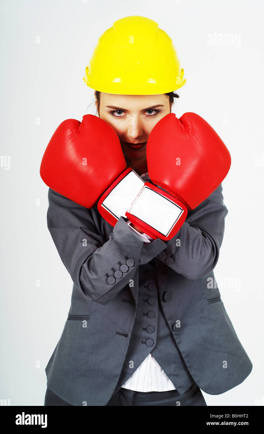 Young businesswoman, manager wearing red boxing gloves and yellow hardhat defending herself Stock Photo