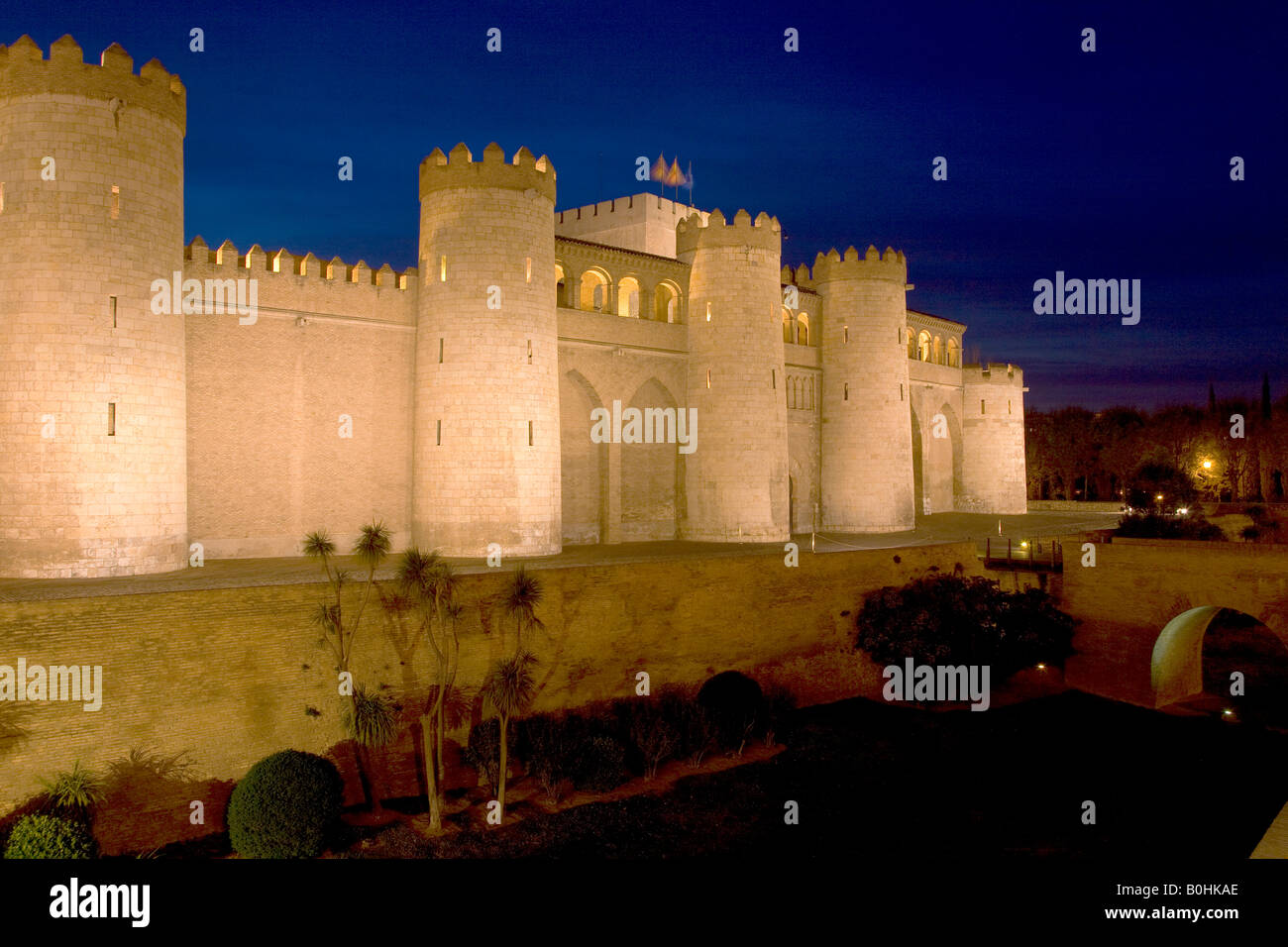 Palacio de Aljaferia palace illuminated at night under floodlights, flags flying over external wall and towers, Moorish archite Stock Photo