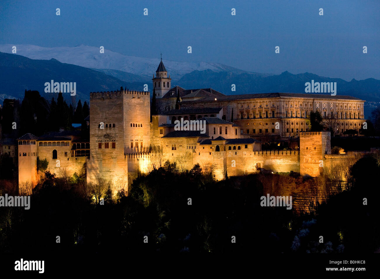 Moorish Alhambra Palace under floodlights at twilight, illuminated at dusk, Sierra Nevada at back, viewed from the Mirador San  Stock Photo