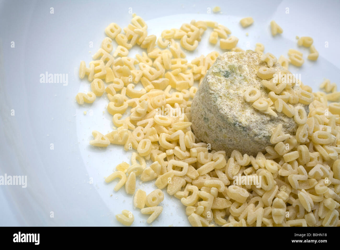 Lump of dry instant soup on a plate surrounded by alphabet noodles Stock Photo