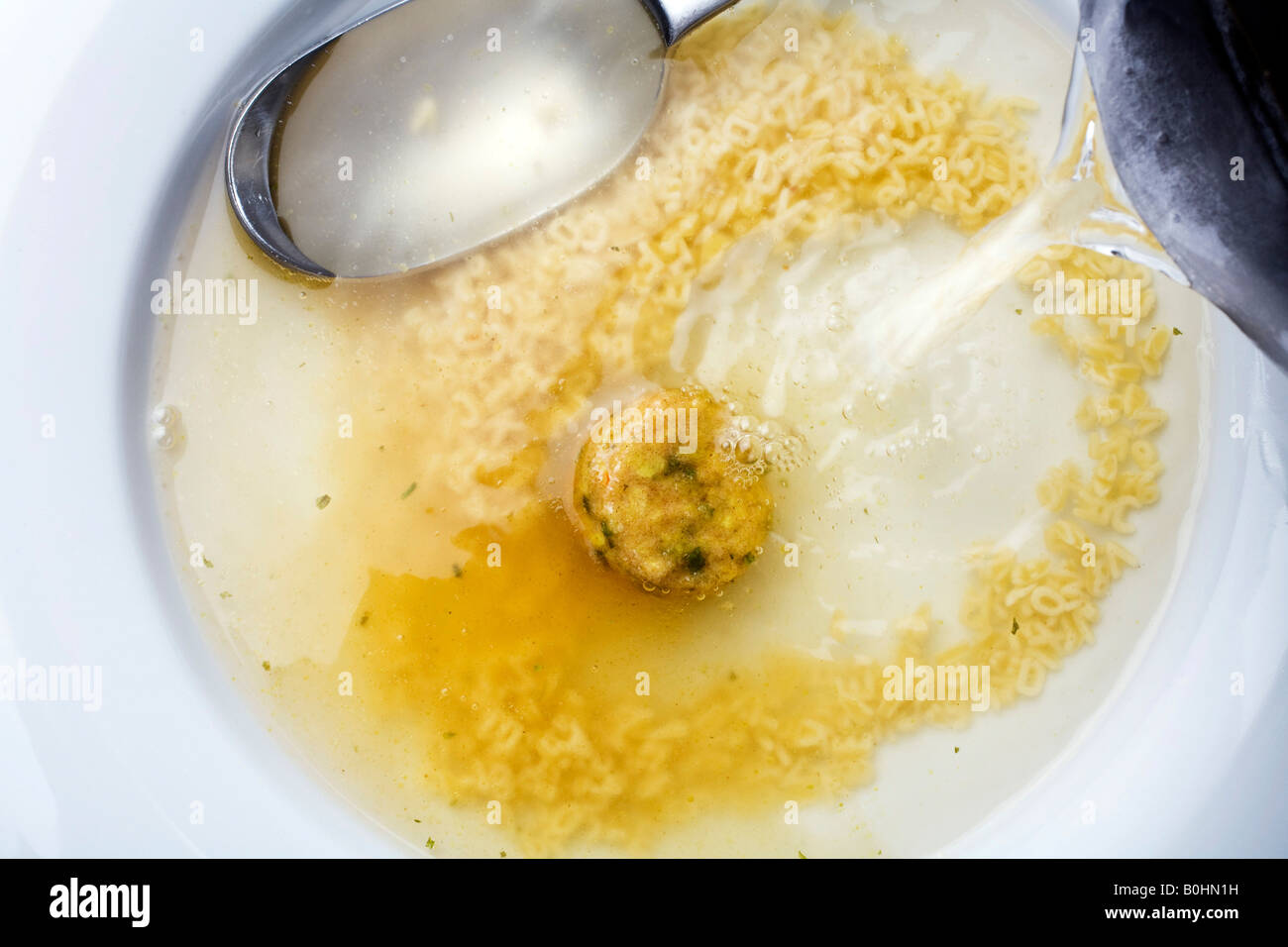 Lump of dry instant soup on a plate surrounded by alphabet noodles, hot water being added Stock Photo