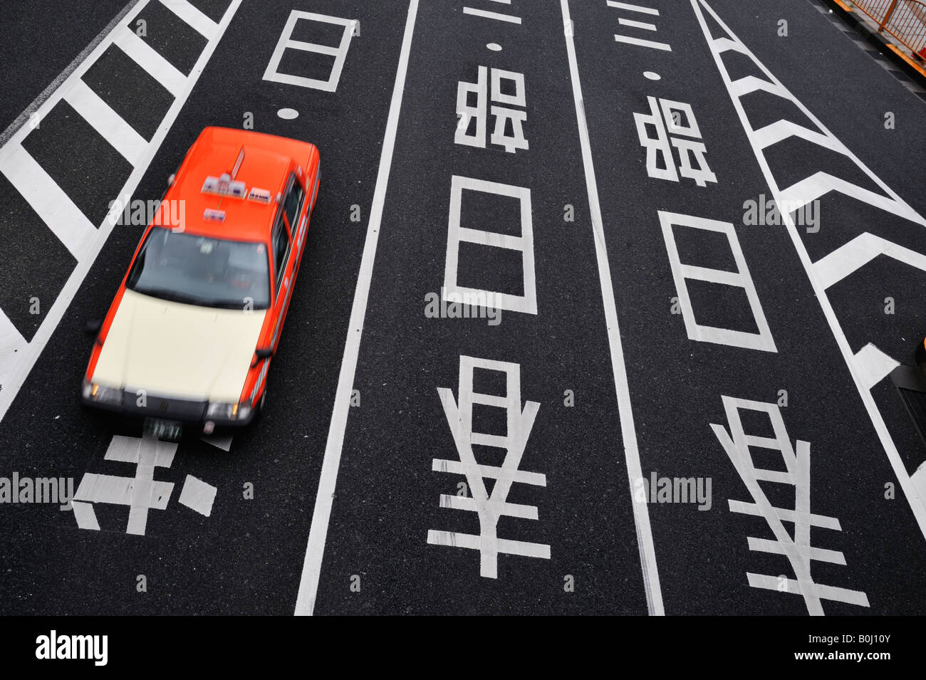 Red taxi drives over road lane direction markings in Kanji writing in Tokyo Japan Stock Photo
