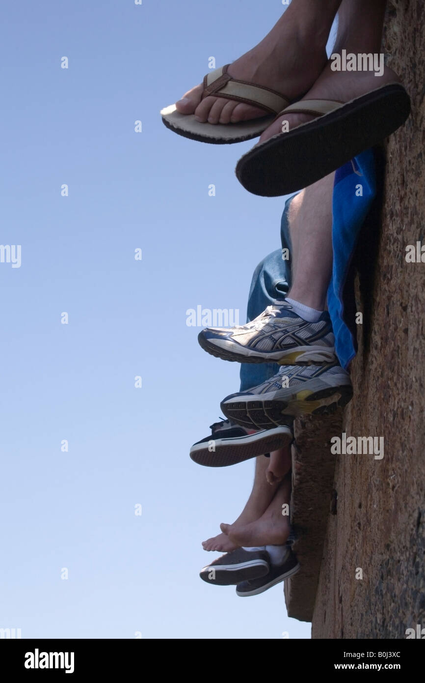 A view looking up at peoples legs and feet, hanging over the edge of a cement wall. Stock Photo