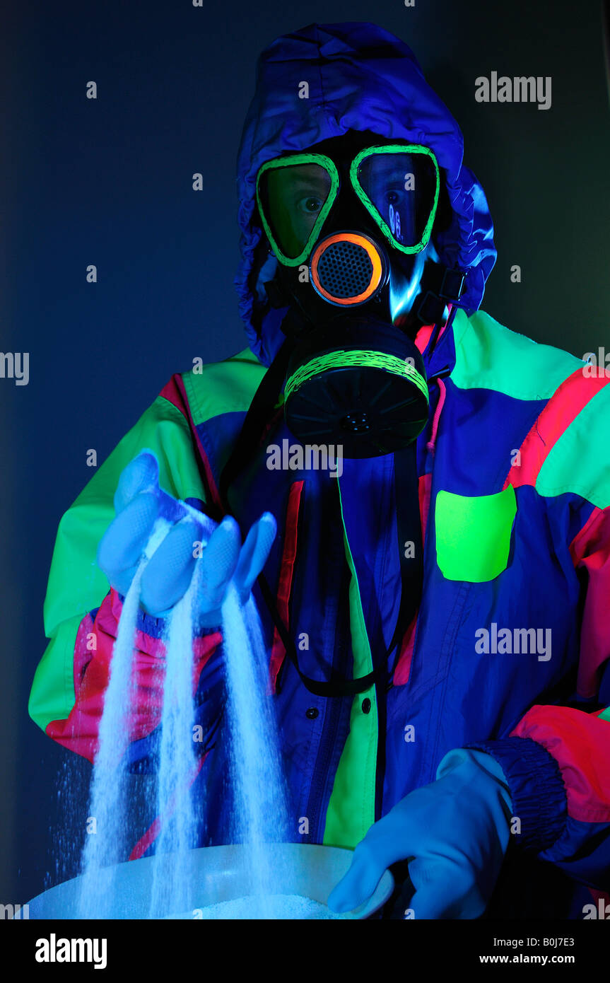 Hooded man in gas mask with gloves in hazmat suit sifting dangerous white crystals under UV light Stock Photo