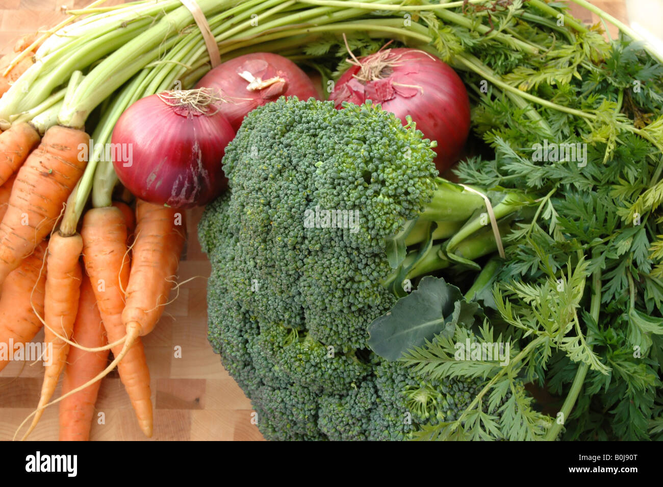 Bunches of carrots broccoli and red onions on a cutting board Stock Photo