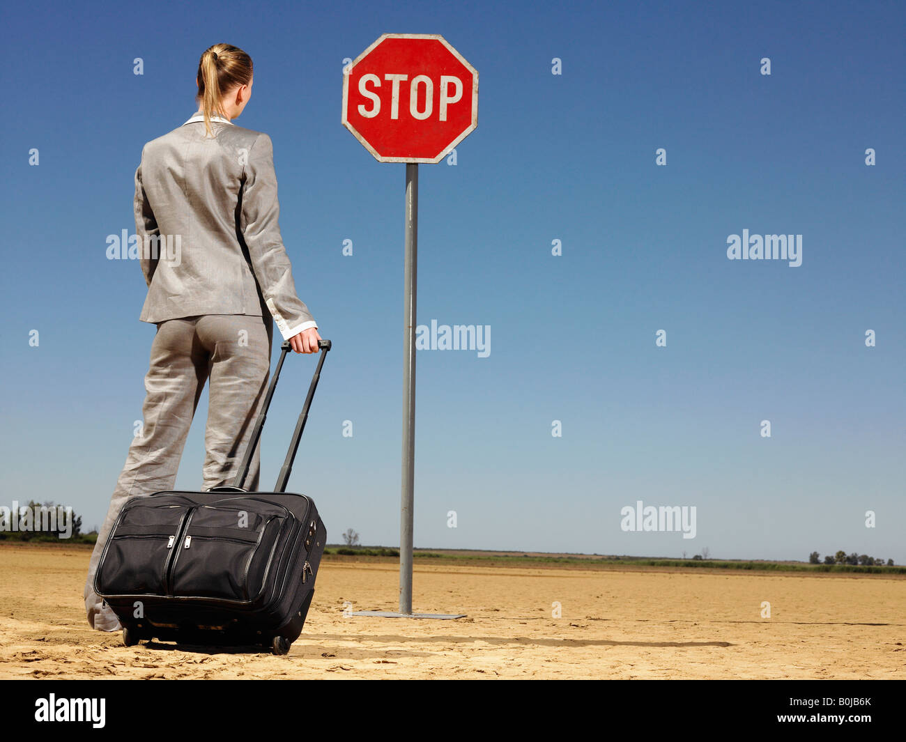Businesswoman in Desert Looking at Stop Sign Stock Photo