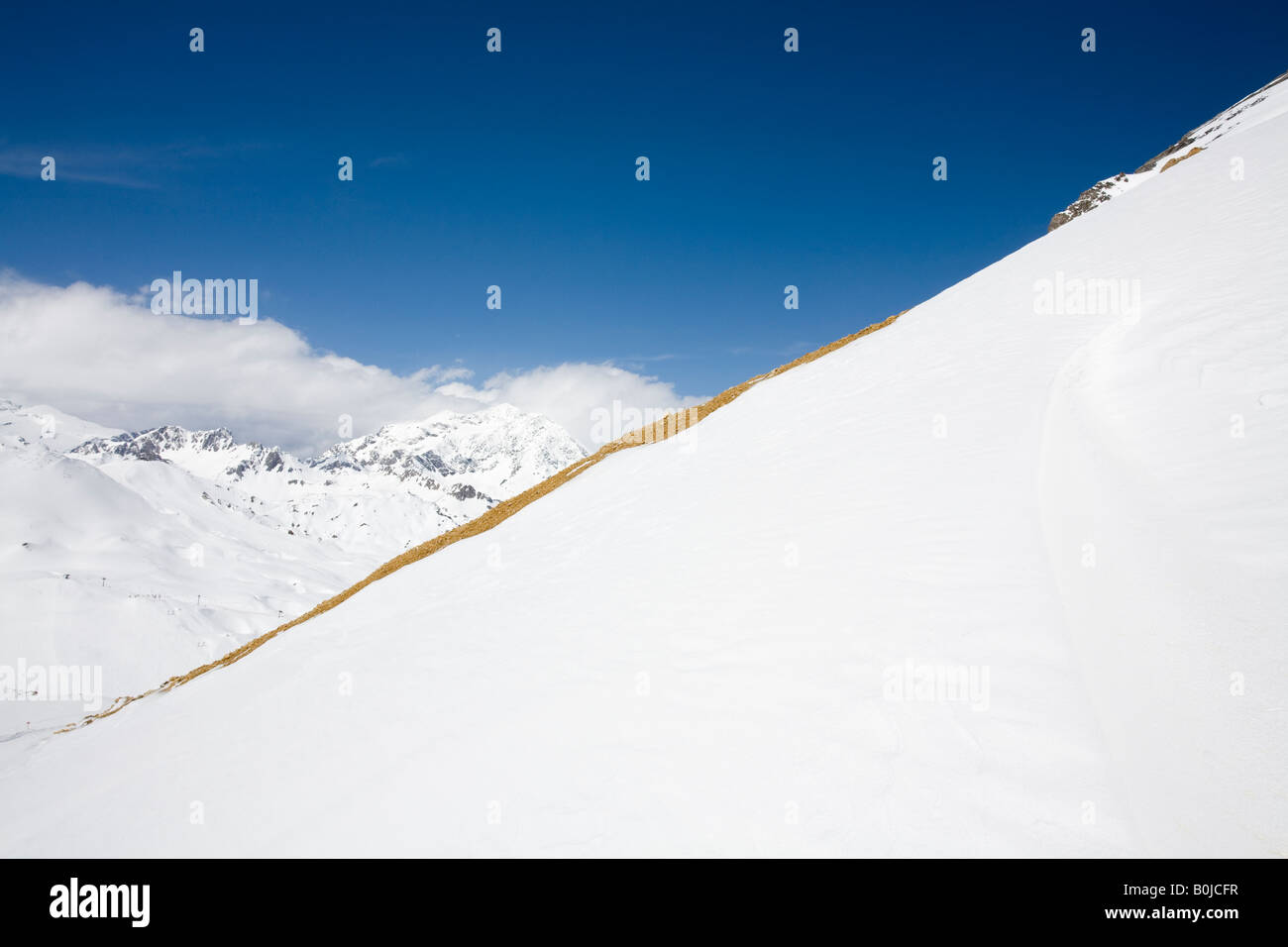 Diagonal line of orange brown rocks divides a blue-sky landscape of snow-capped Val-d'Isère mountains Stock Photo
