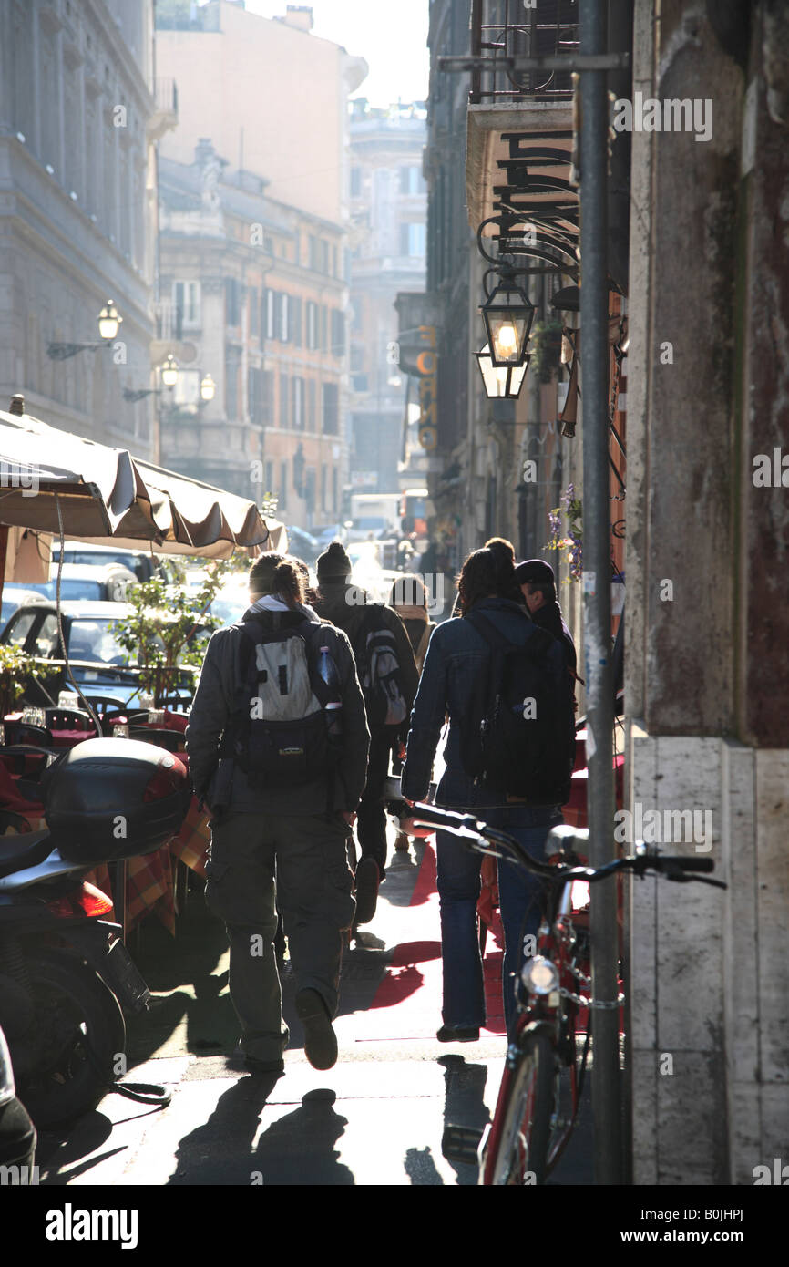 Group of young backpackers tourists backlit walking down street in Rome