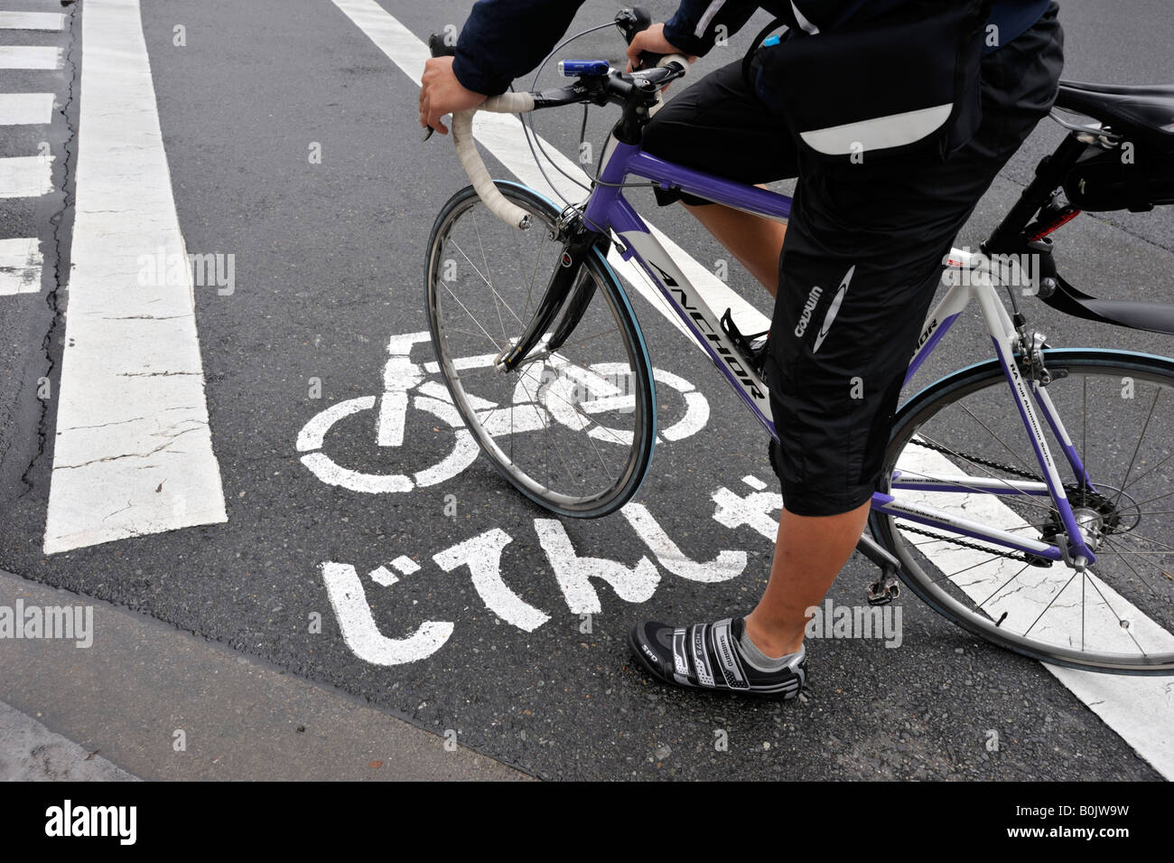 Cyclist waits to cross intersection along designated cycle lane in central Tokyo Stock Photo