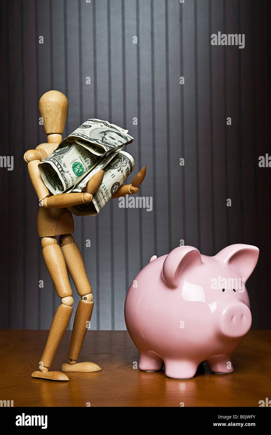 Manikin carrying a ball of money towards a piggy bank Stock Photo