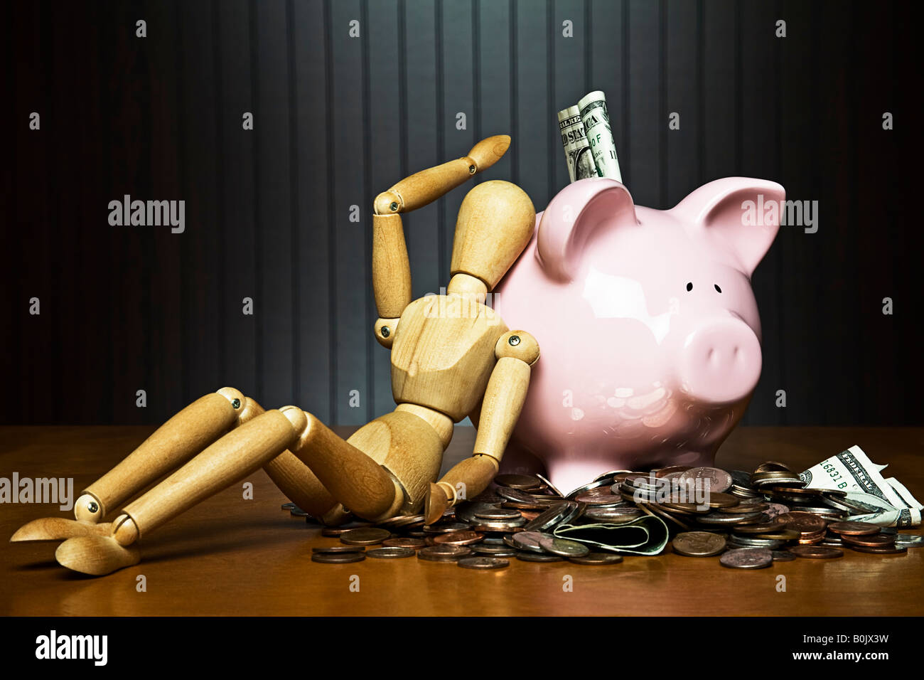 Manikin leaning against a piggy bank surrounded by money Stock Photo