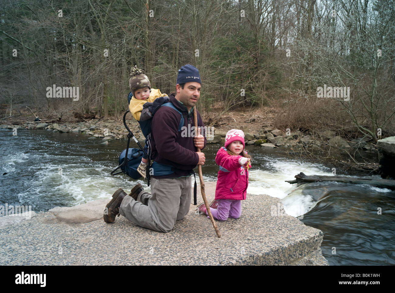 A Man hiking with his two small children near a river in the forest Stock Photo