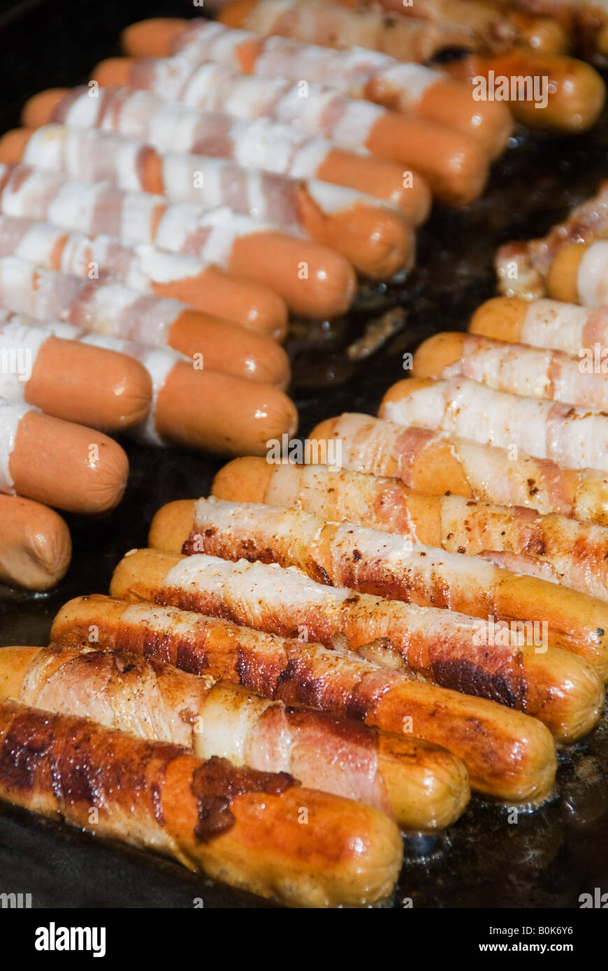 Bacon wrapped hot dogs sizzle on the grill Stock Photo