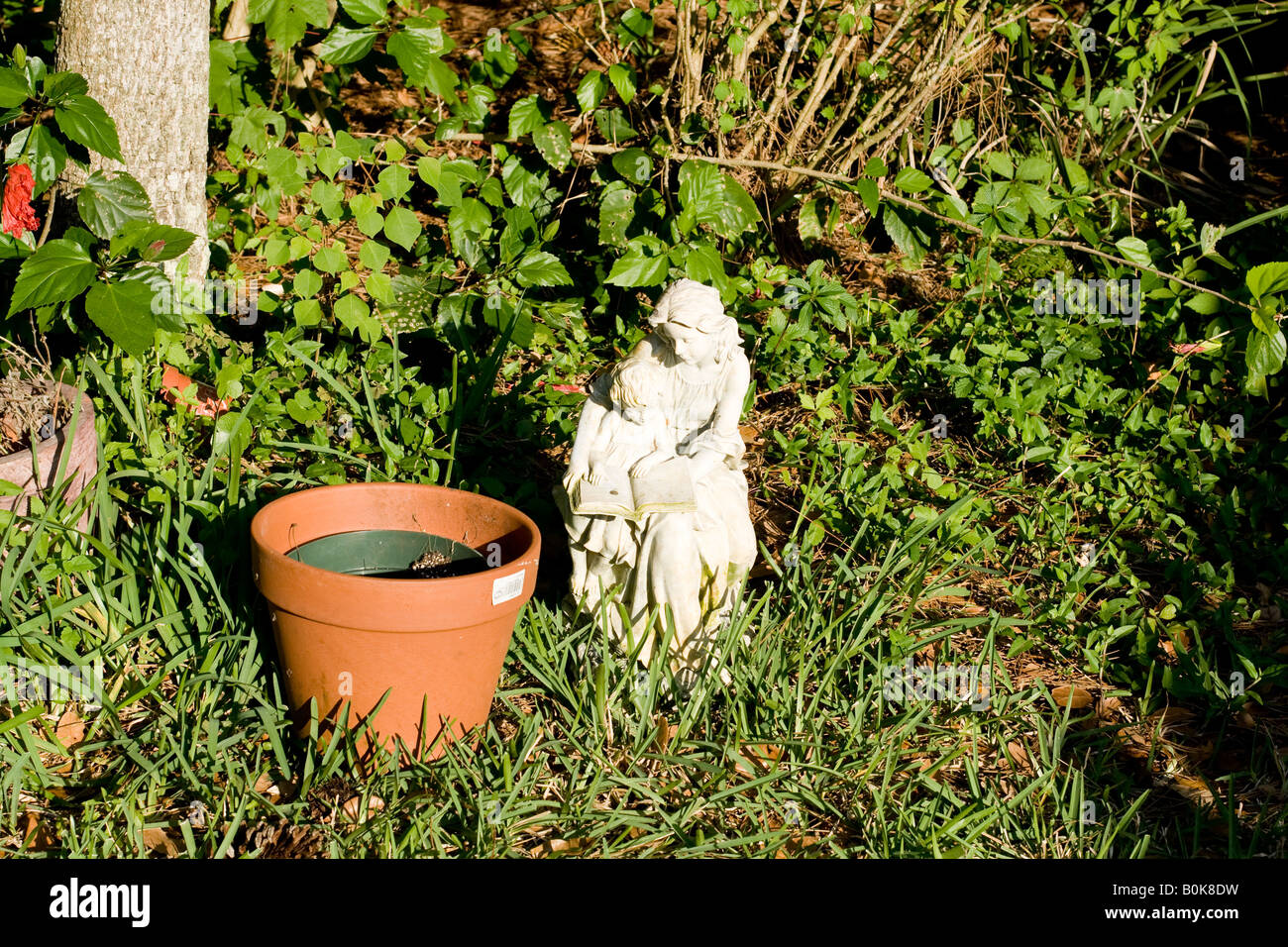 Small white statuette of a woman and a child next to a flower pot in green brush in Ponte Vedra Beach, Florida Stock Photo