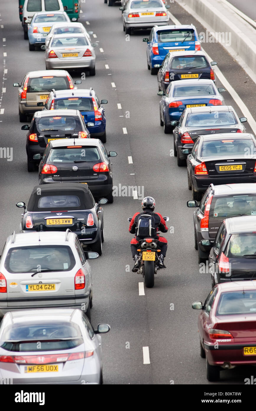 Motorcyclist slips through two lanes of traffic congestion on M25 motorway London United Kingdom Stock Photo