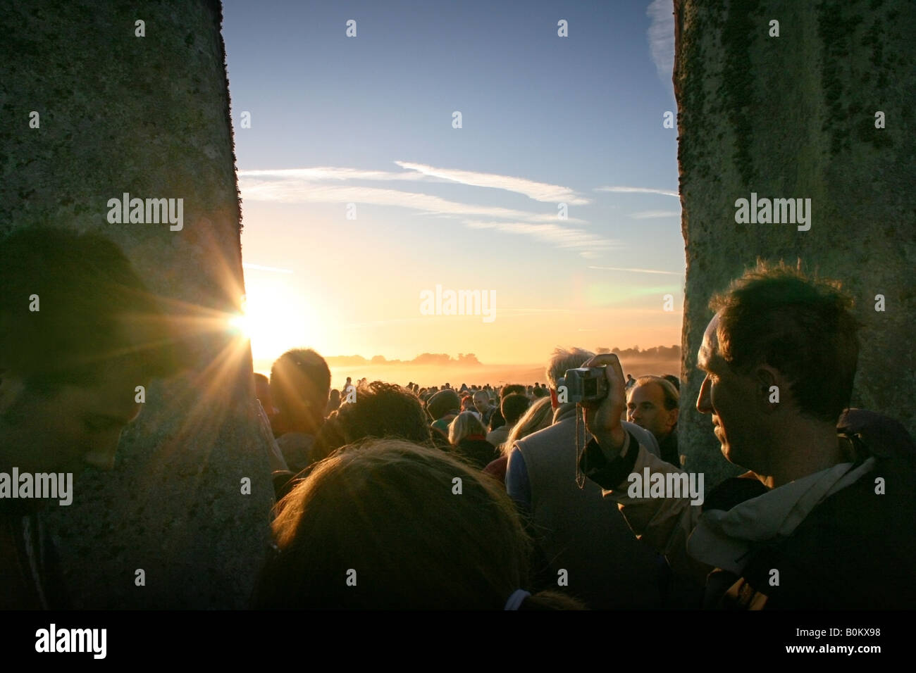 Sunlight bursts in through the stones, dazzling the crowds of people who have waited the night at Stonehenge Summer Solstice. Stock Photo