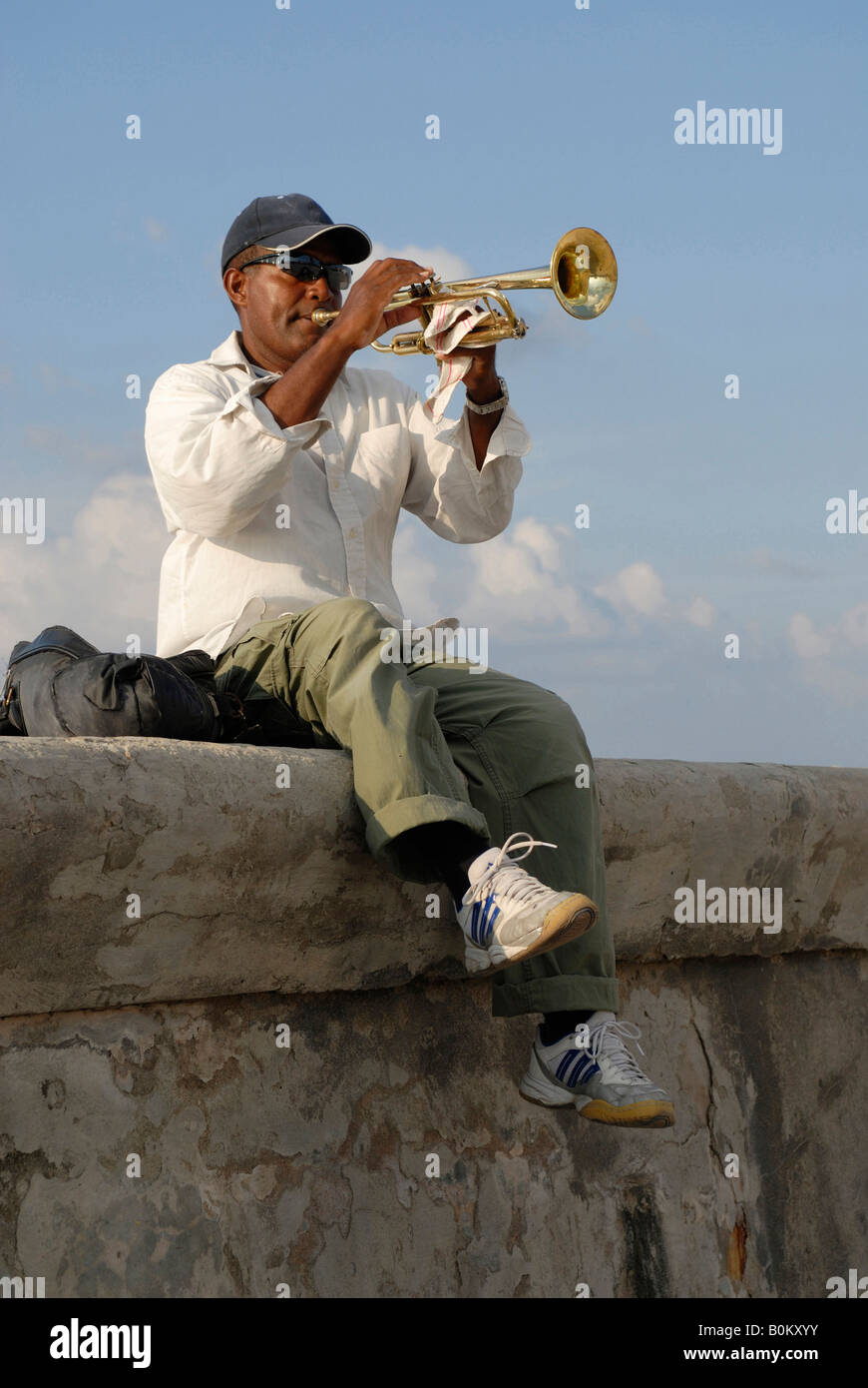 A middle aged man sitting on a wall and playing trumpet at the Malecon Boulevard in Havana Cuba April 2007 Stock Photo