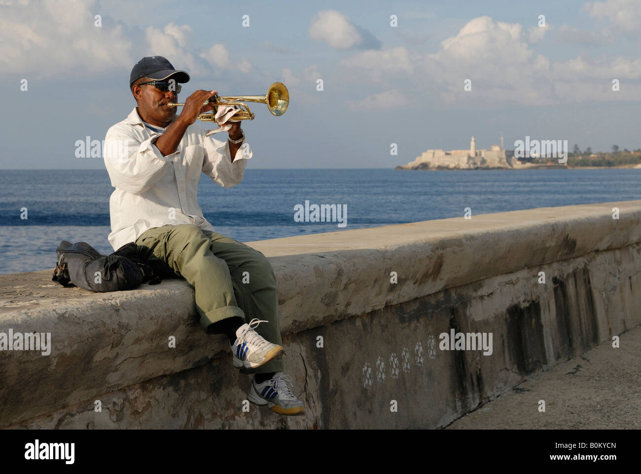 A middle aged man sitting on a wall and playing trumpet at the Malecon Boulevard in Havana Cuba April 2007 Stock Photo