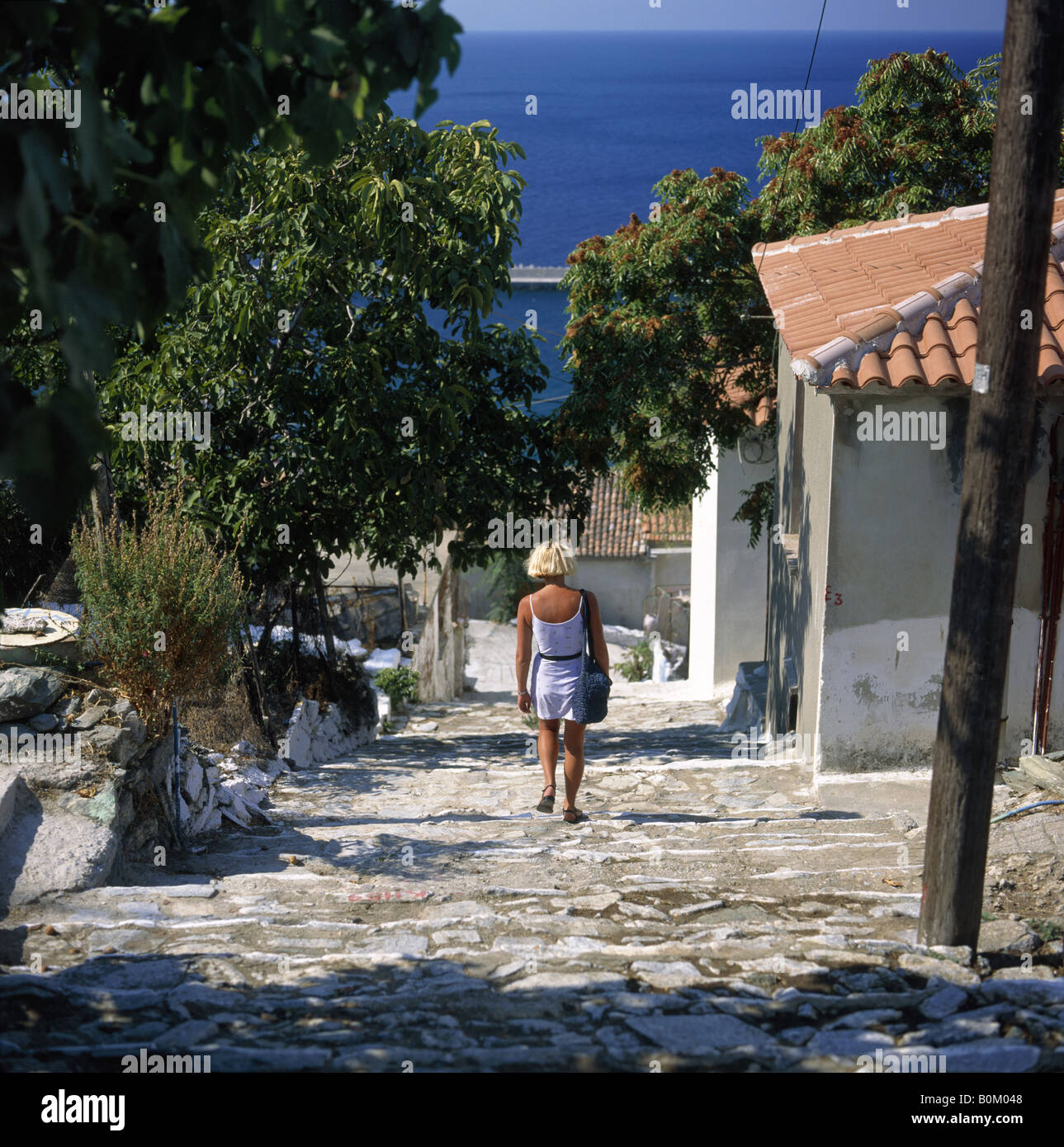 Aegean island. Cobbled street steps. Houses. View to sea. Woman walking. Stock Photo