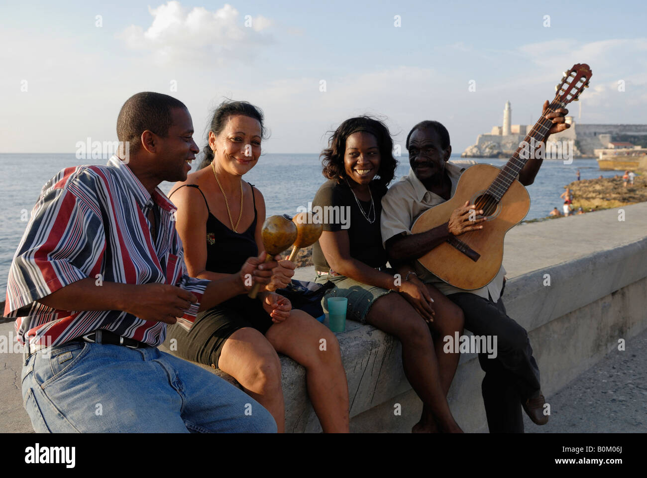 Two women and two men sitting on a wall and playing their instruments at the Melacon Boulevard in Havana Cuba April 2007 Stock Photo
