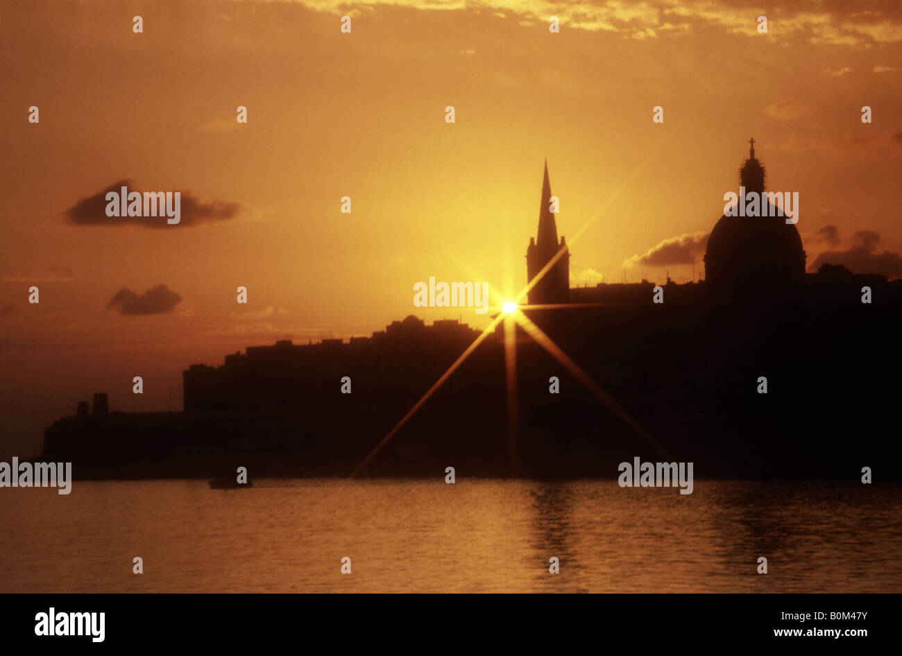 Sun rising over silhouette of buildings. Sea. Orange sky Stock Photo ...