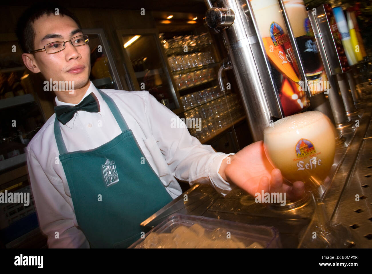 Chinese barman serves a Belgian Leffe beer in Le Roy d’Espagne bar. Grand Place, Bruxelles. Belgium Stock Photo