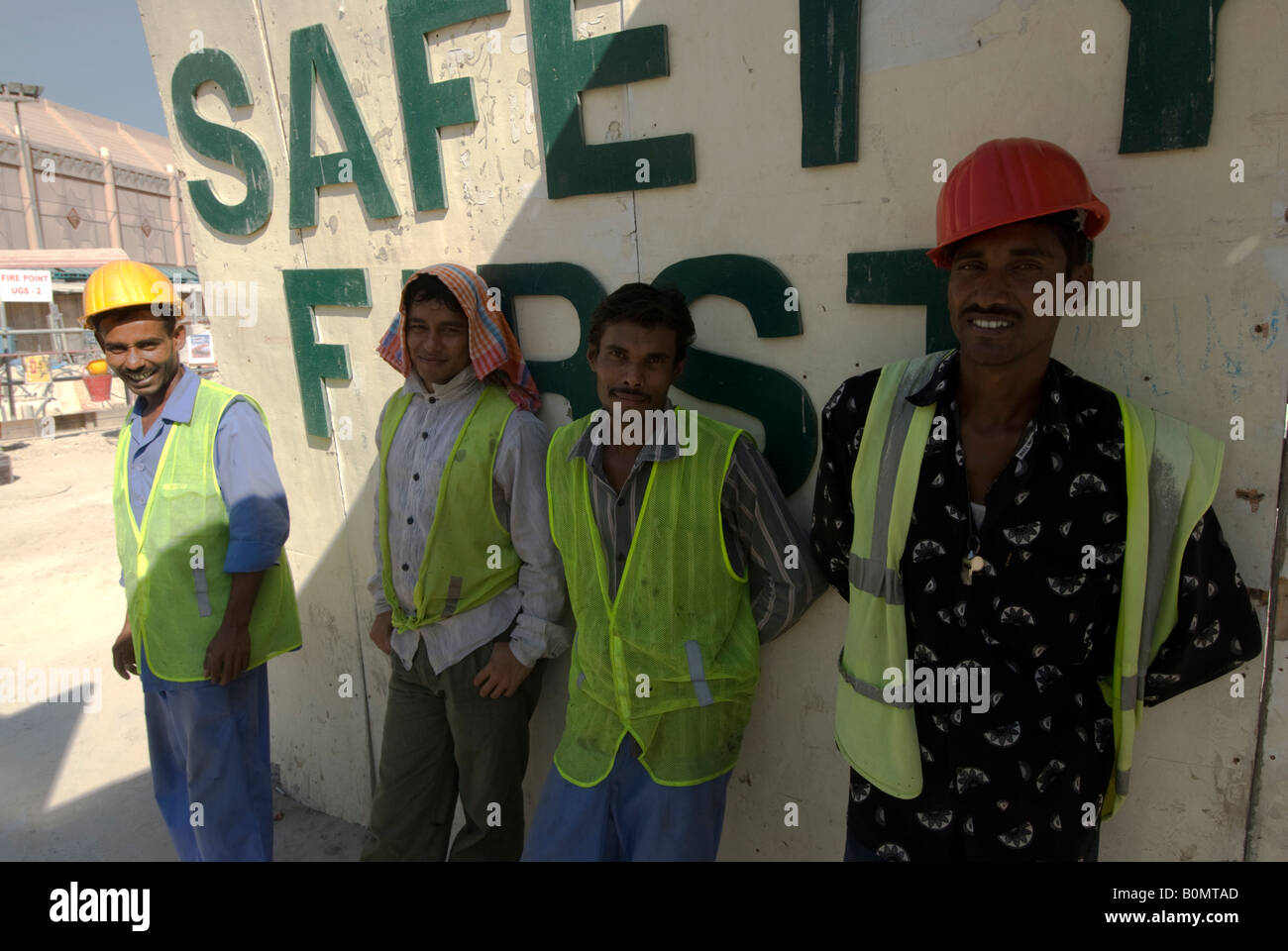 Four migrant workers take a break in the shade against a wall where is written: Safety first, Dubai, United Arab Emirates. Stock Photo