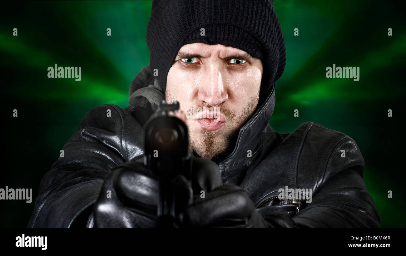 Portrait of an undercover agent or delinquent dressed in black leather and balaclava hat firing handgun in the camera Stock Photo