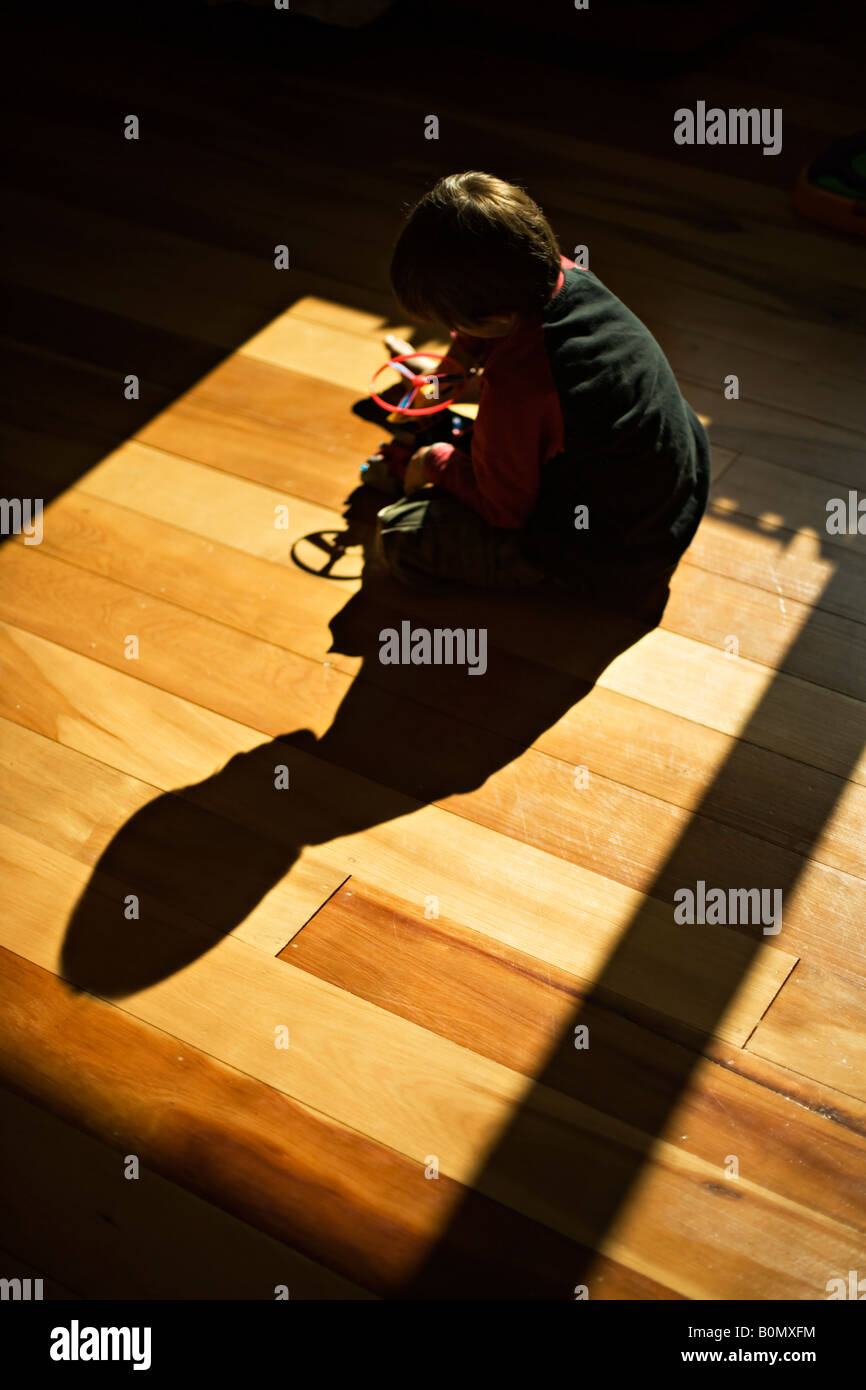 Boy aged six plays with toy plastic helicopter on floor of his room with full sun streaming through the window Stock Photo