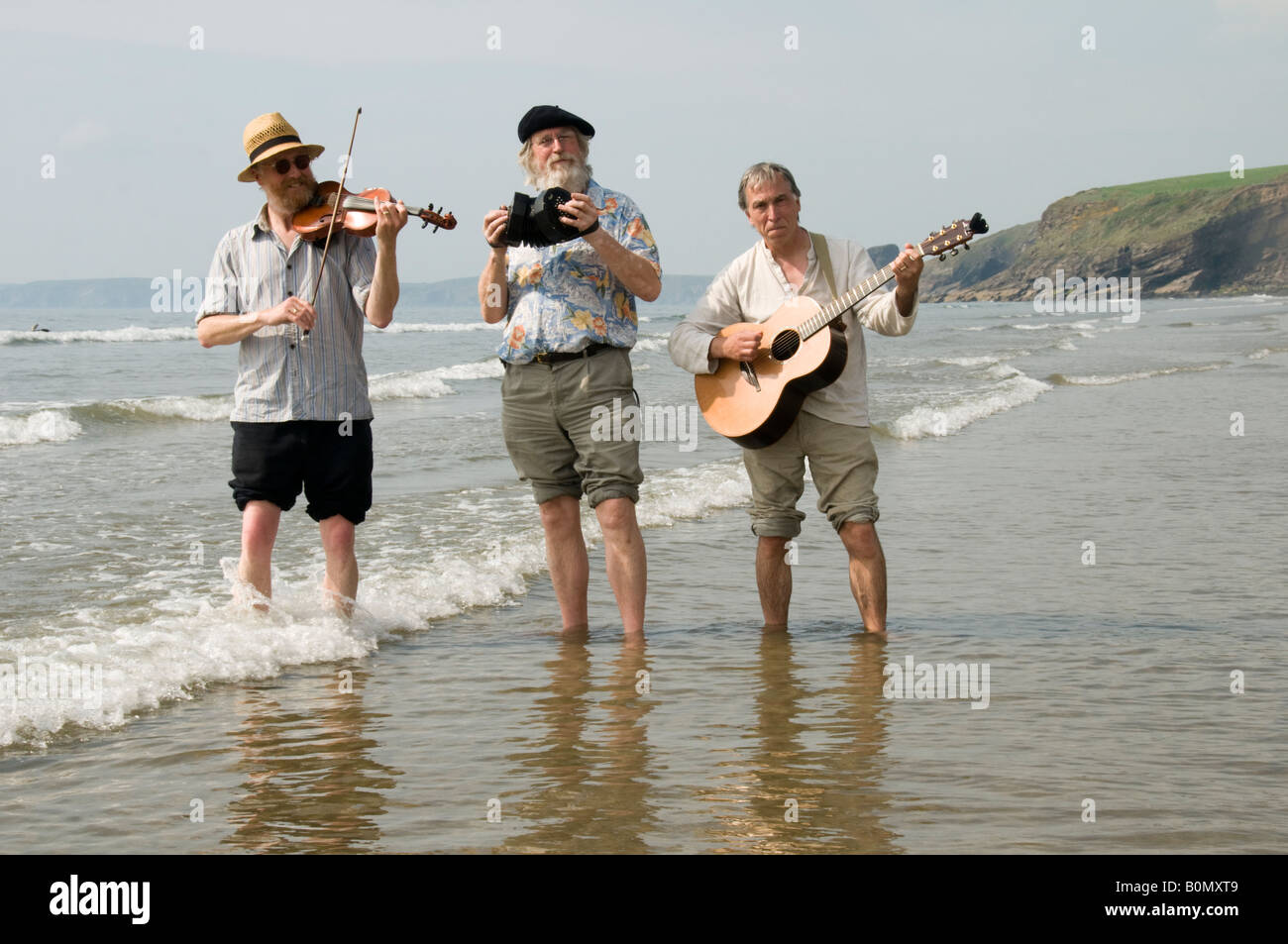 Three traditional acoustic folk musicians playing music on the beach