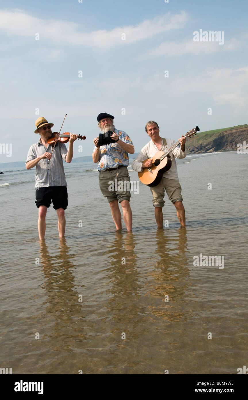 Three traditional acoustic folk musicians playing music on the beach
