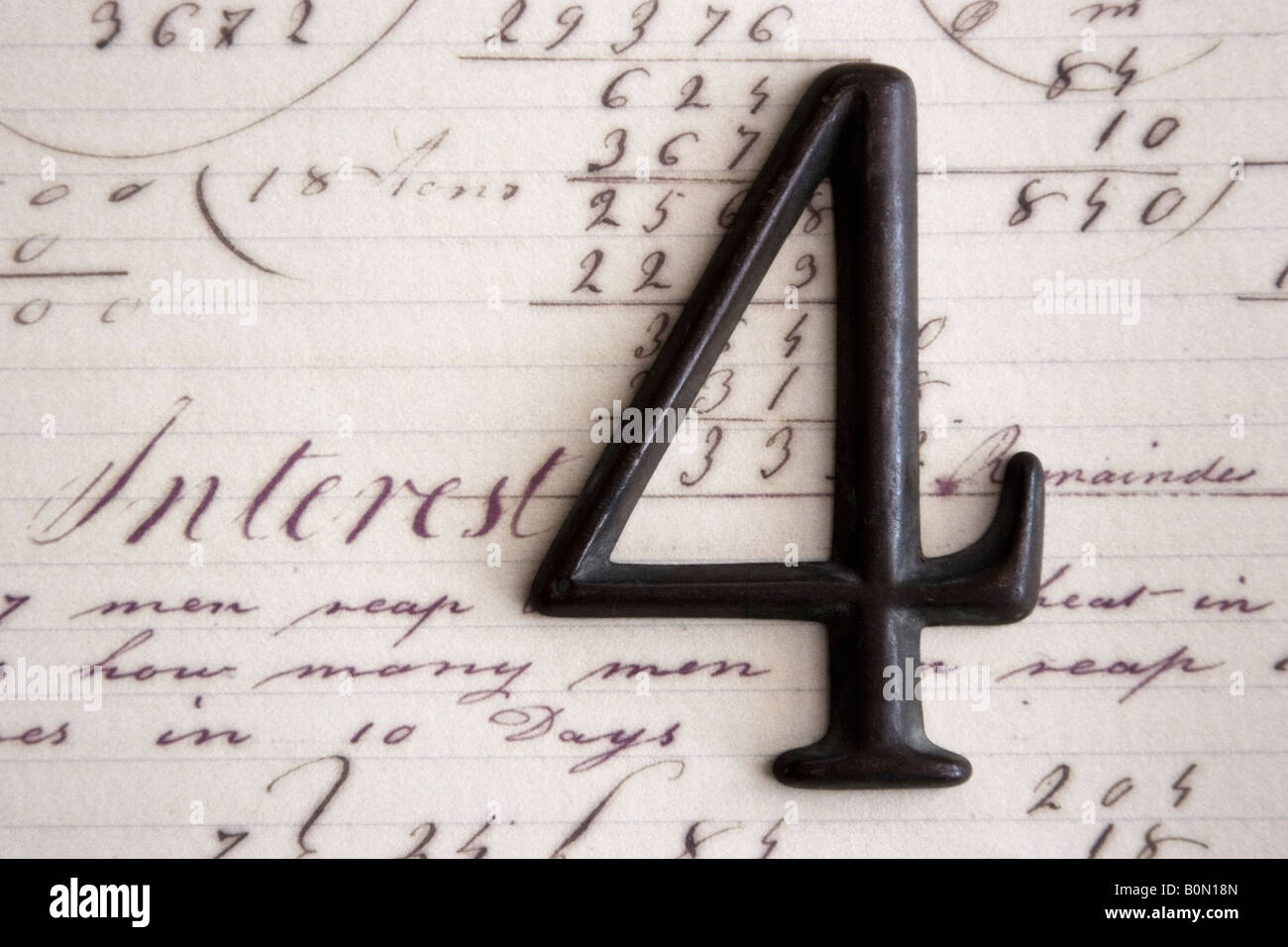 A dark metal number four pictured on paper containing other numbers and mathematical operations. Stock Photo