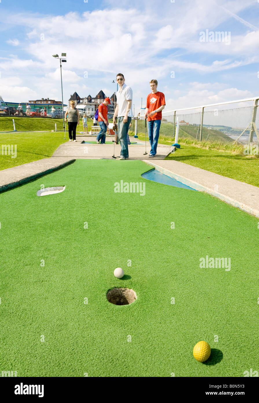 Two mid 20s men playing crazy golf in Whitby, North Yorkshire, UK Stock Photo