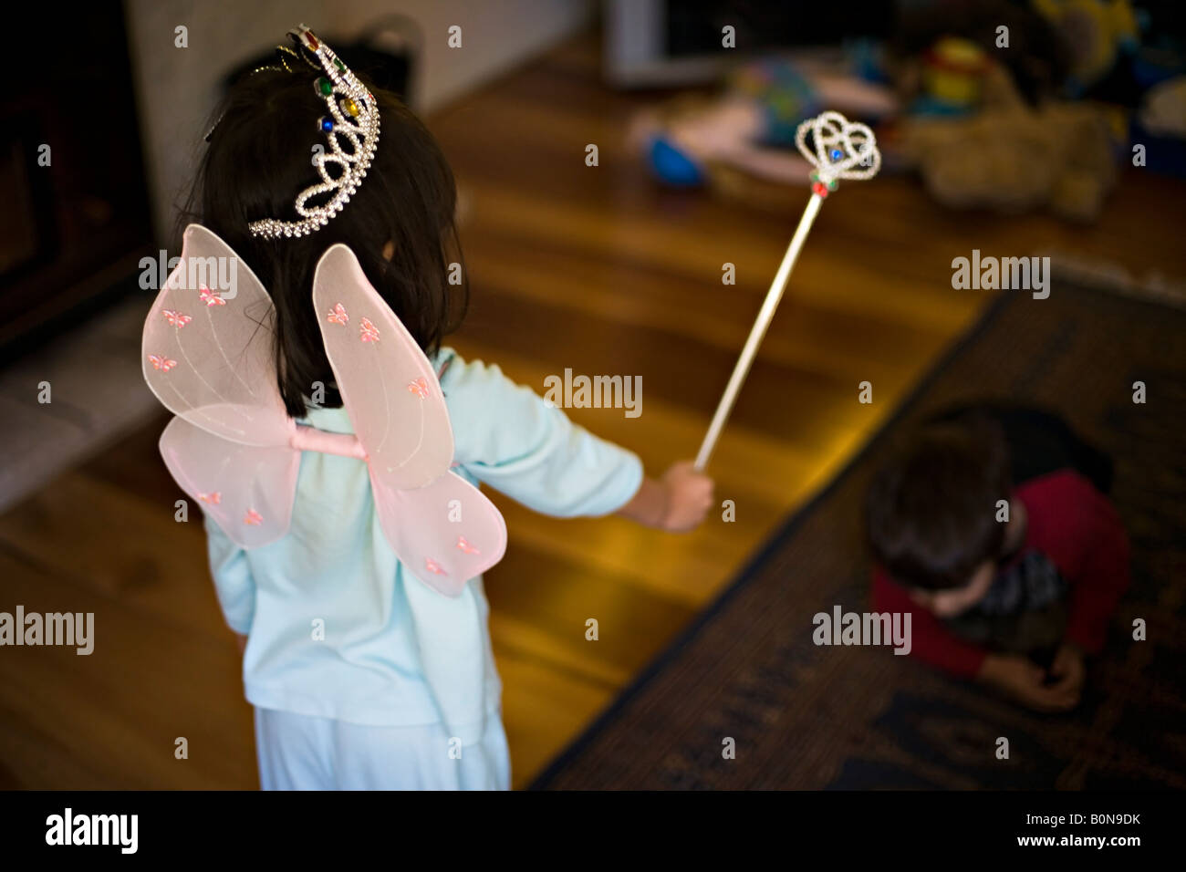 Four year old girl in fairy costume casts a spell on her six year old brother kneeling in the shadows Stock Photo
