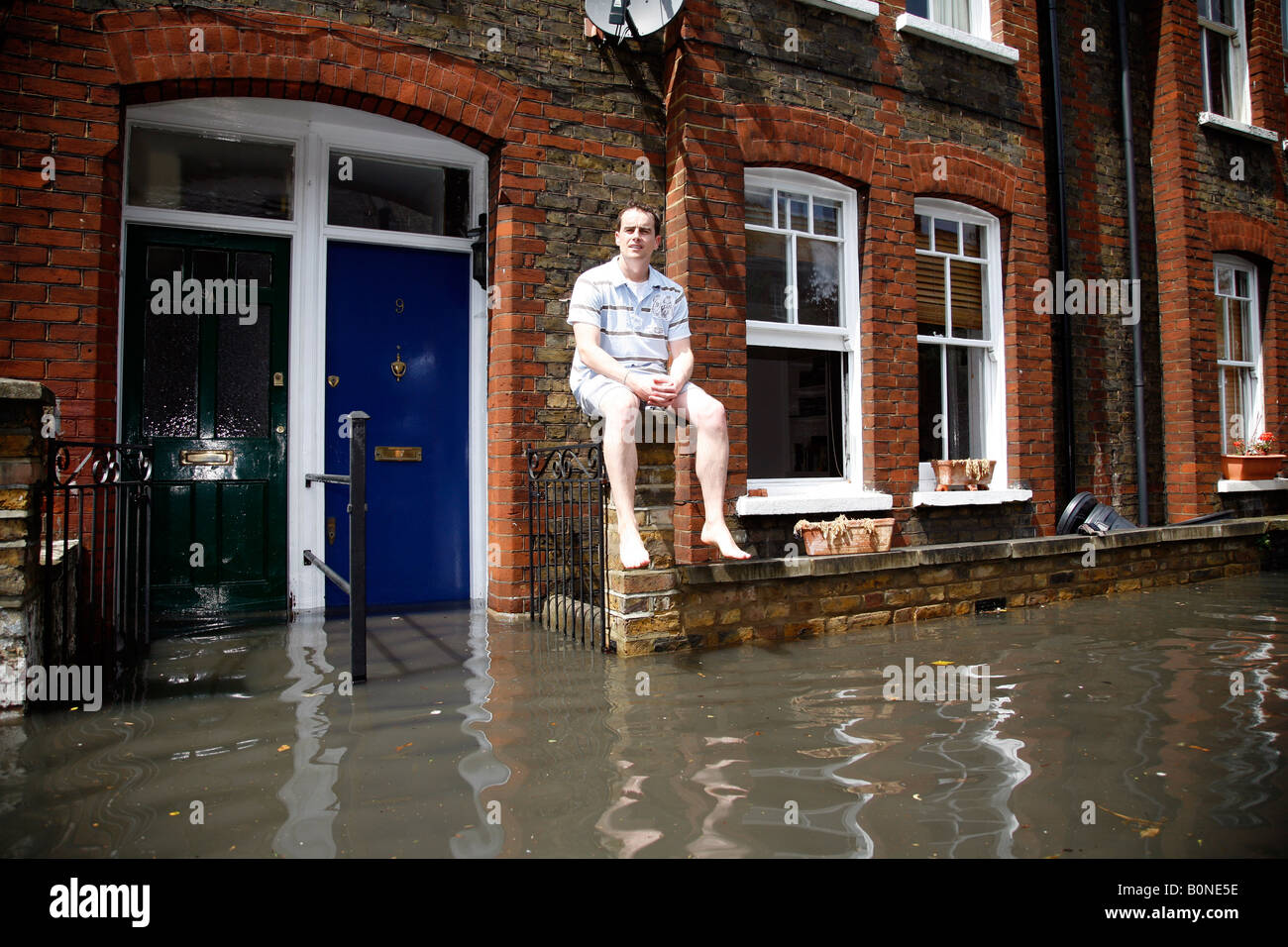 Young man sitting on a wall and surveying a flooded street, urban ...