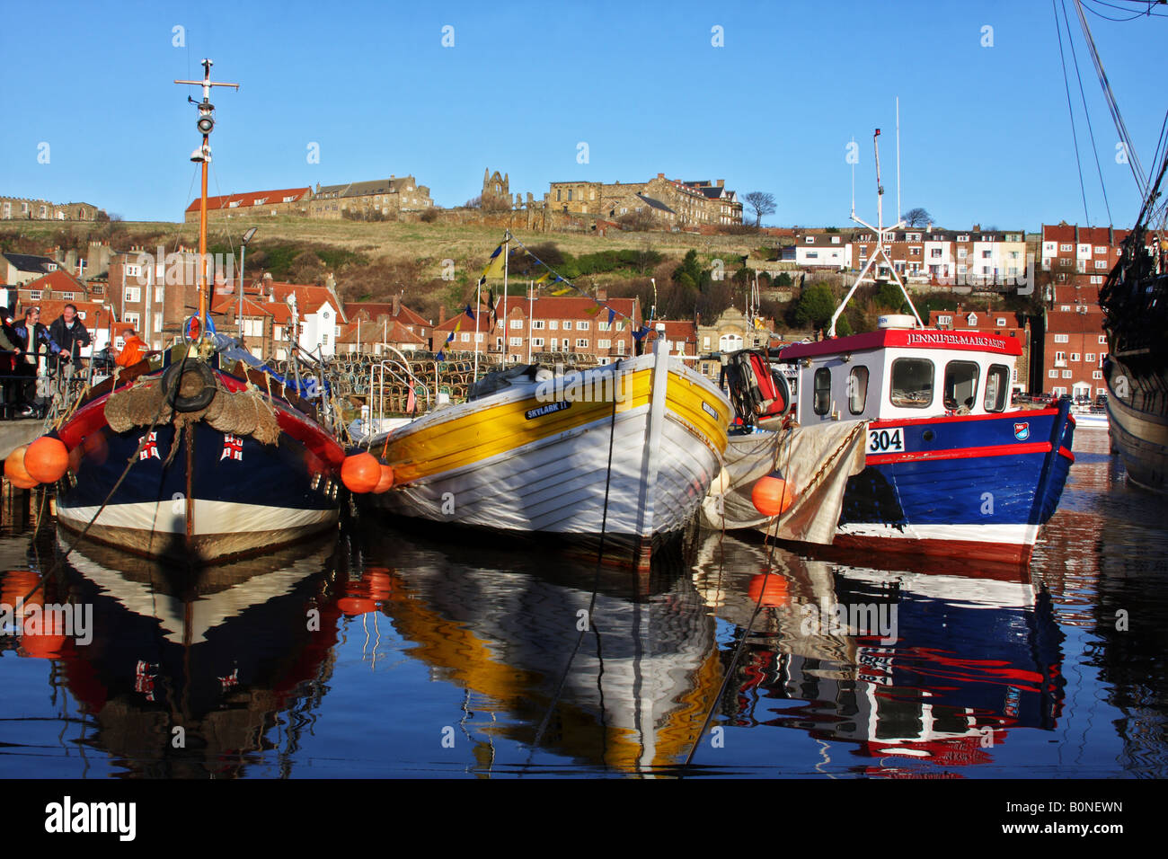 Working fishing boats in Whitby Harbour, with abbey behind and against a blue sky. Stock Photo