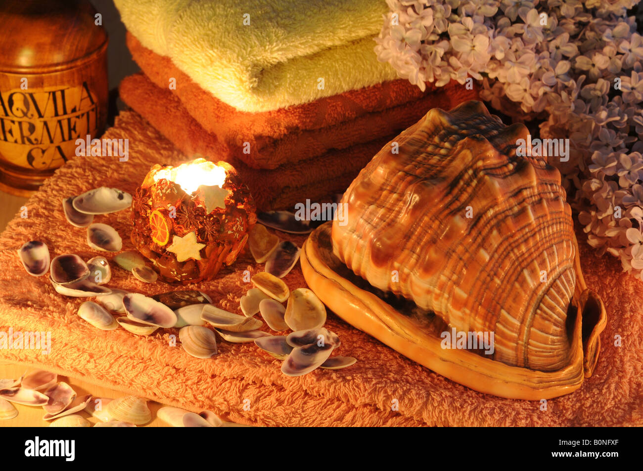 Red and yellow towels conch sea shells and lilac flowers lit by candle Stock Photo