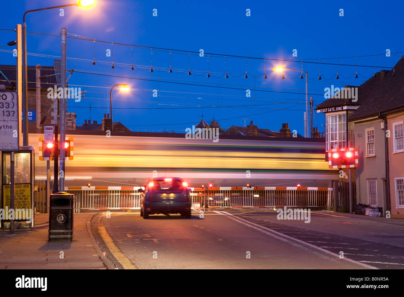 TIME EXPOSURE OF COLCHESTER EAST GATES RAIL CROSSING AT NIGHT WITH A TRAIN PASSING AND THE BARRIERS DOWN Stock Photo