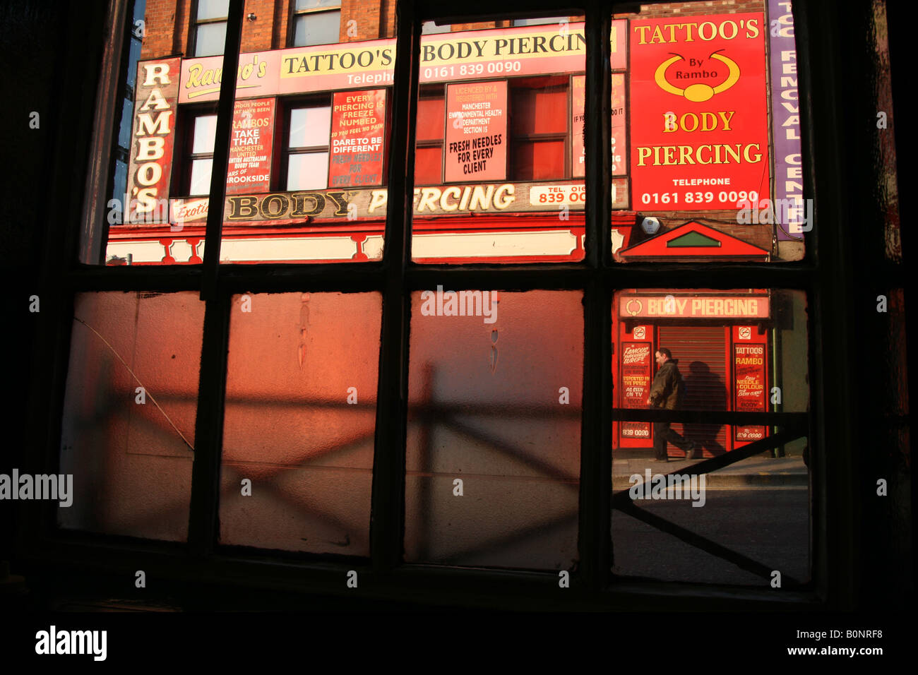 Tattoo Body Piercing Shop framed through a café window in the Northern Quarter  Manchester UK' Stock Photo