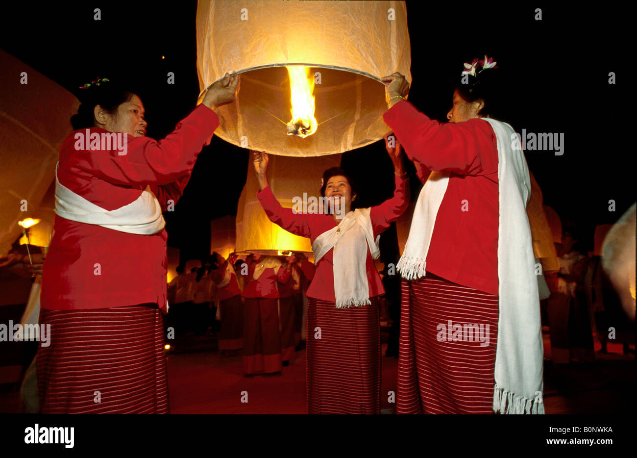 Thai women celebrate Loy Krathong by releasing traditional paper hot air balloon 'kom fai' into the night sky, Mae Jo, Chiang Mai, Thailand Stock Photo