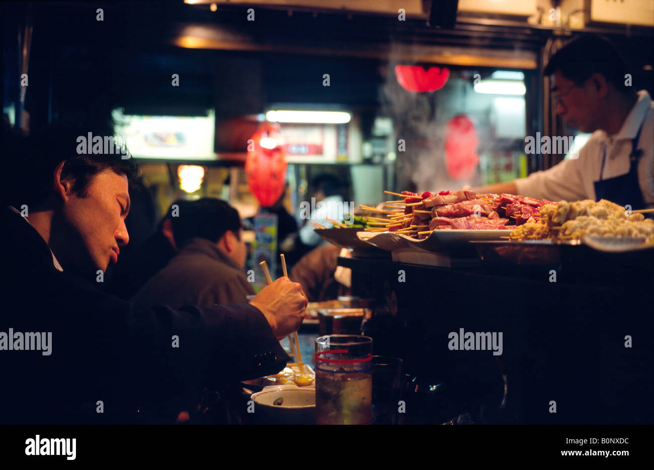Man eating at one of the dimly lit Izakayas serving Yakitori in Shinjuku's Golden Gai area in the Japanese capital of Tokyo. Stock Photo