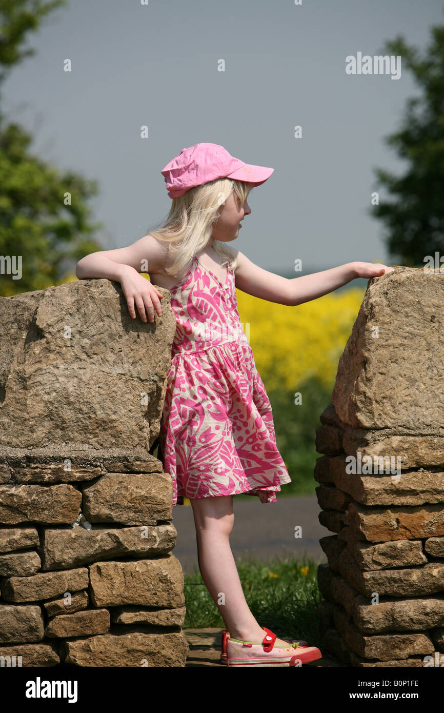 Blonde little girl standing on a dry stone wall with rapeseed in ...