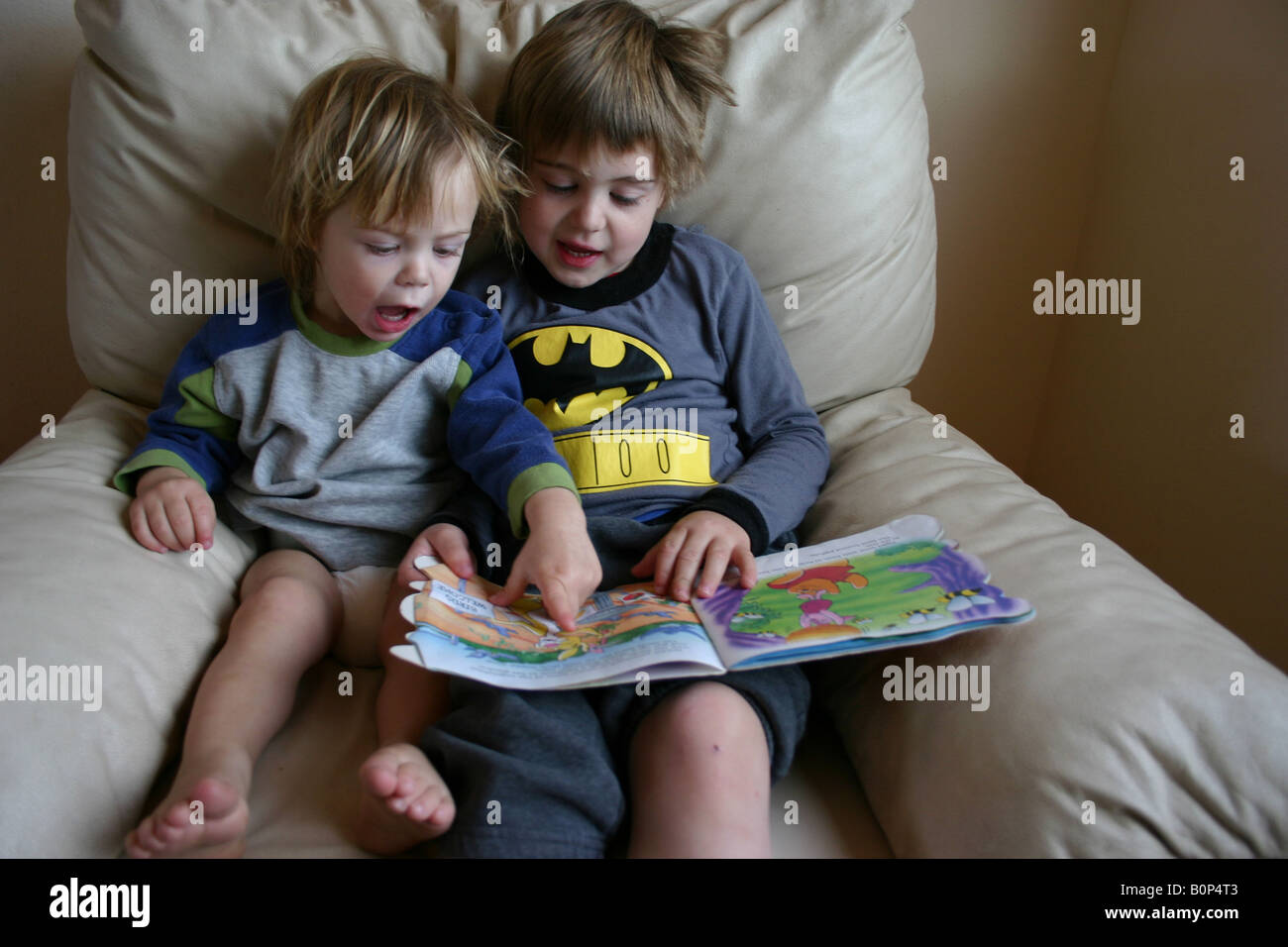 five year old boy reading to two year old younger brother at home Stock