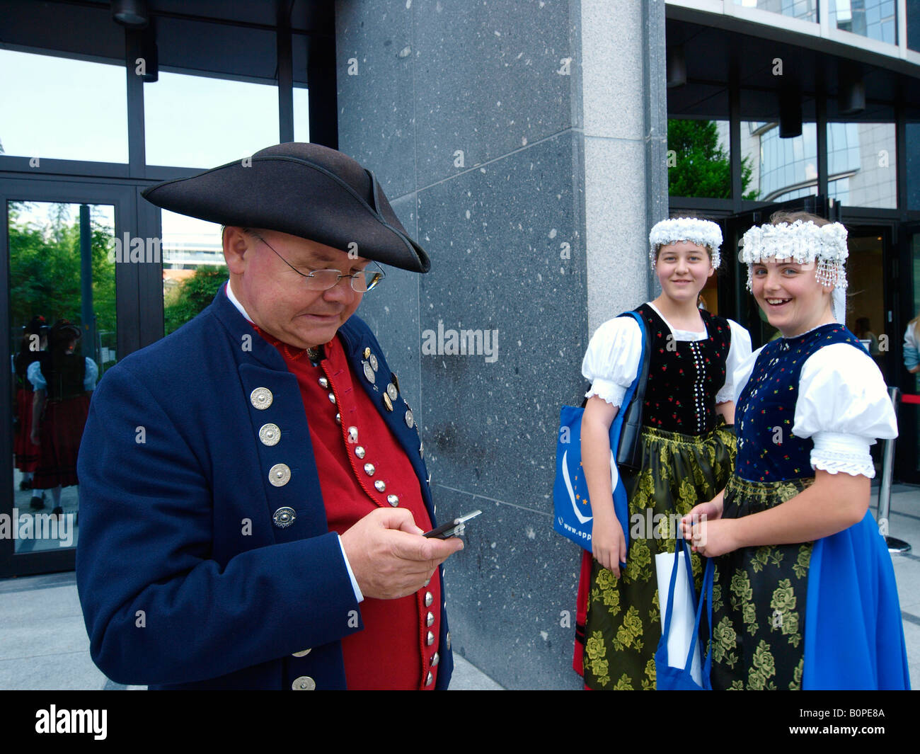 Man in historic costume using cellphone mobile phone with two girls laughing EU parliament Brussels Belgium Stock Photo